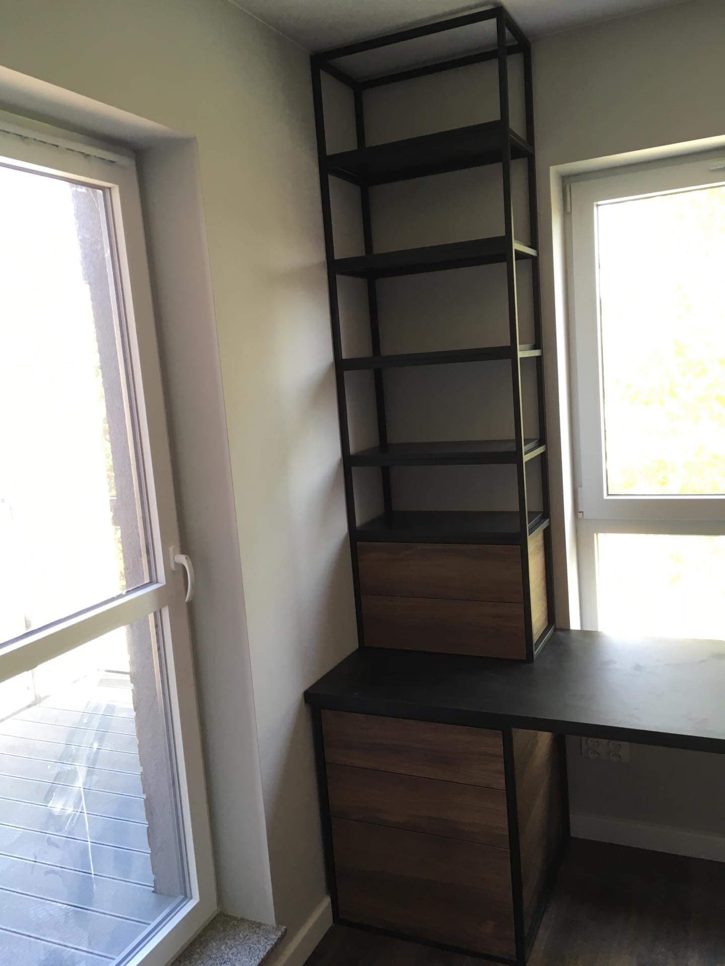 Metalowa konstrukcja regału z drewnianymi szufladami wkomponowana w biurko, widok z boku przy oknie.