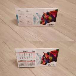 Dwa kalendarze biurkowe piramidki z kolorową grafiką głowy tygrysa w stylu pop-art, rok 2019, widok z bliska na drewnianym blacie.