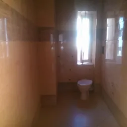 Wykończona łazienka z beżowymi płytkami imitującymi marmur, jasnym oknem z zasłoną i toaletą w rogu.