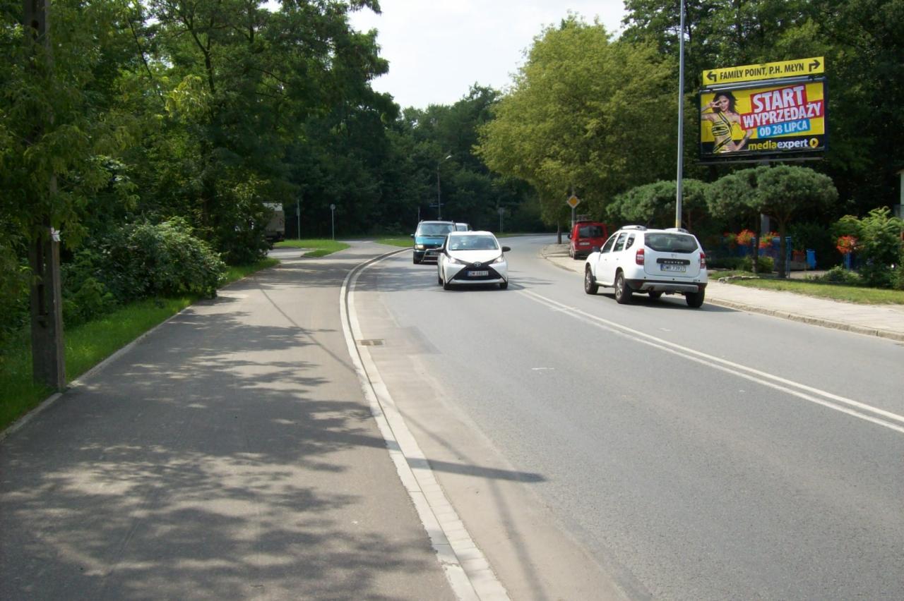 Billboard z reklamą wyprzedaży na tle ulicy z samochodami i zielenią drzew.