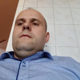 Mężczyzna w błękitnej koszuli, ujęcie z dołu, widoczna część kafelkowanej ściany i fragment sufitu. Oświetlenie dzienne.