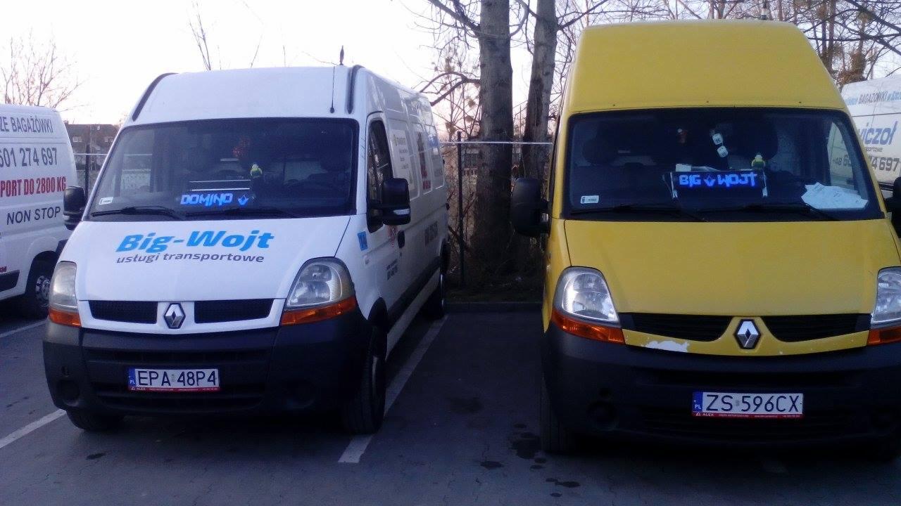 Dwa busy Renault Master zaparkowane obok siebie: biały z niebieskim logo firmy transportowej 'Big-Wojt' i żółty z podświetlanym napisem 'Big Wojt' na desce rozdzielczej. W tle widoczne drzewa...