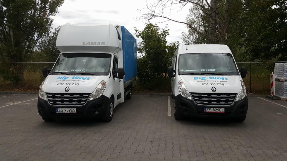 Dwa białe busy firmy transportowej Big-Wojt zaparkowane obok siebie na parkingu z kostki brukowej, jeden z plandeką w kolorze niebieskim. Widoczne numery rejestracyjne ZS 989ES i ZS 829EL.