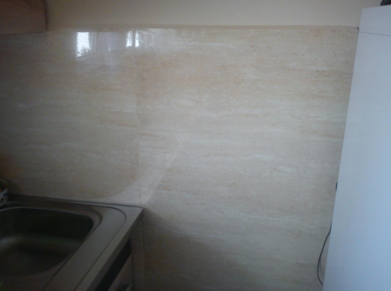 Beżowe płytki imitujące marmur na ścianie nad zlewem w kuchni, z widocznym fragmentem zlewu i szafki.