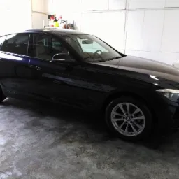 Błyszczący, ciemny samochód BMW po umyciu, widoczny z boku na tle garażu z pralką i środkami czystości.