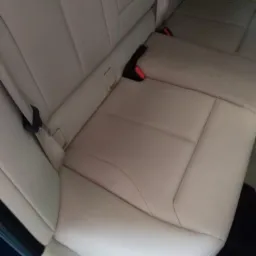 Jasna, skórzana tylna kanapa samochodu z widocznymi pasami bezpieczeństwa i zagłówkami.