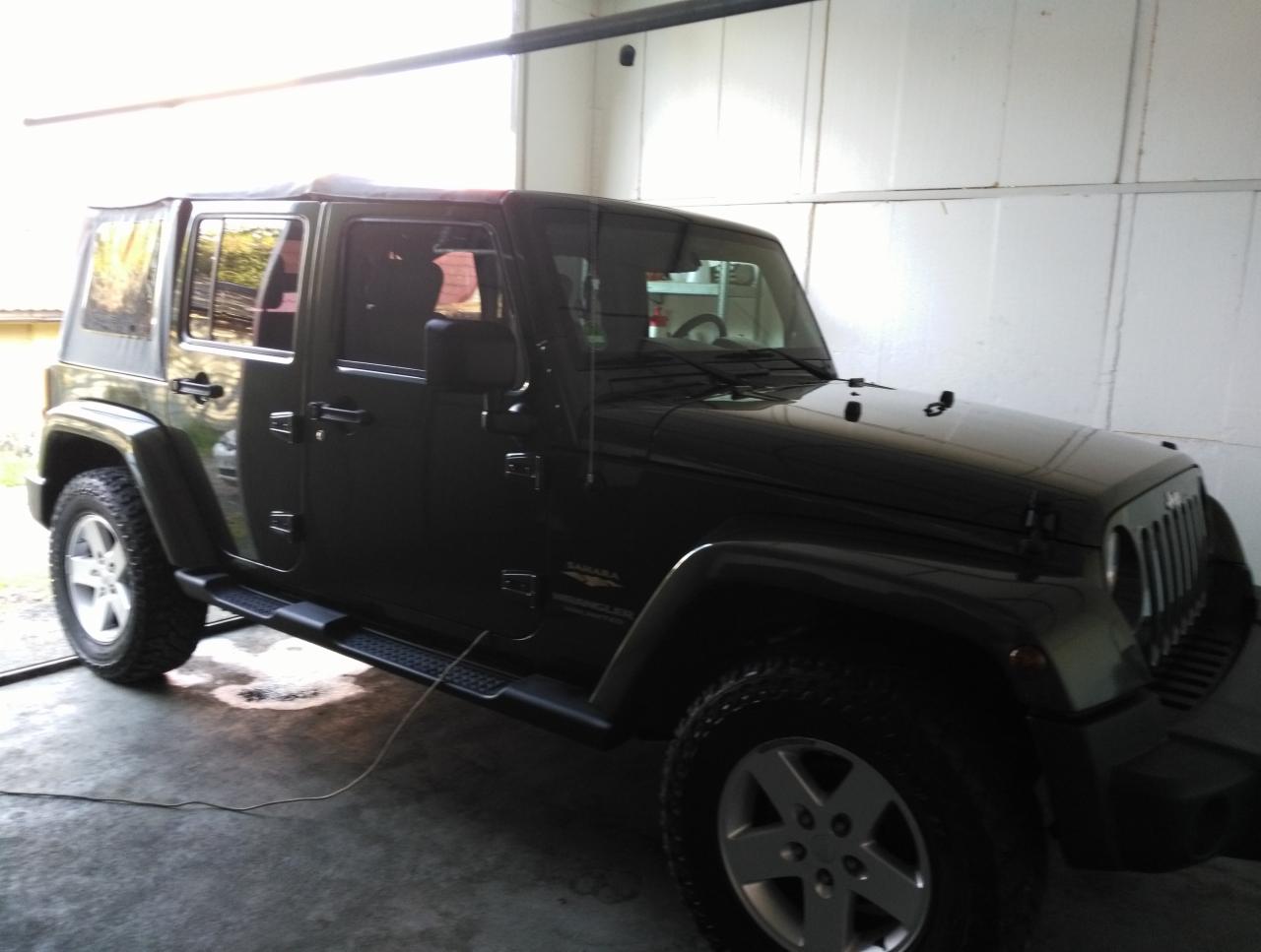 Ciemnozielony Jeep Wrangler Sahara zaparkowany w garażu z widocznym kablem na podłodze.