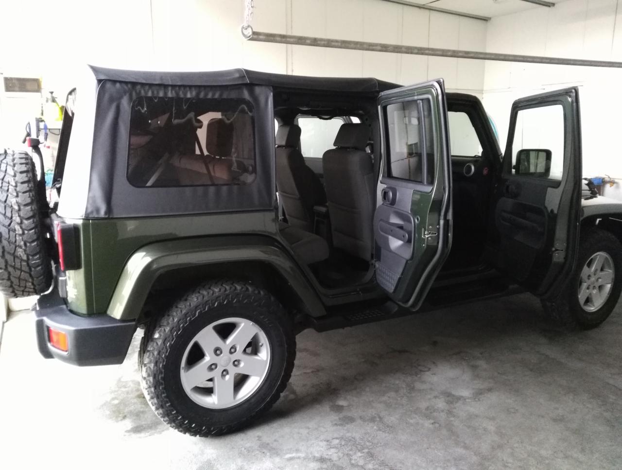 Zielony Jeep Wrangler z otwartymi drzwiami i czarnym miękkim dachem, zaparkowany w garażu.