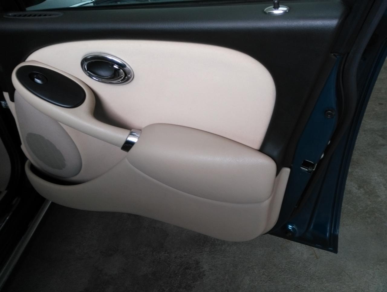 Wnętrze samochodu: beżowy panel drzwi z chromowanymi akcentami uchwytu i klamki, widoczny głośnik w panelu, ciemnozielona karoseria.