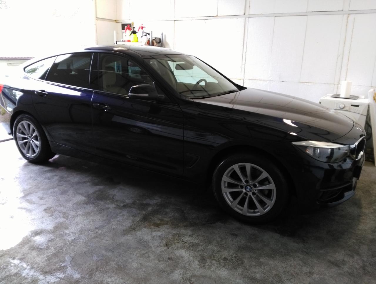Błyszczący, ciemny samochód BMW po umyciu, widoczny z boku na tle garażu z pralką i środkami czystości.