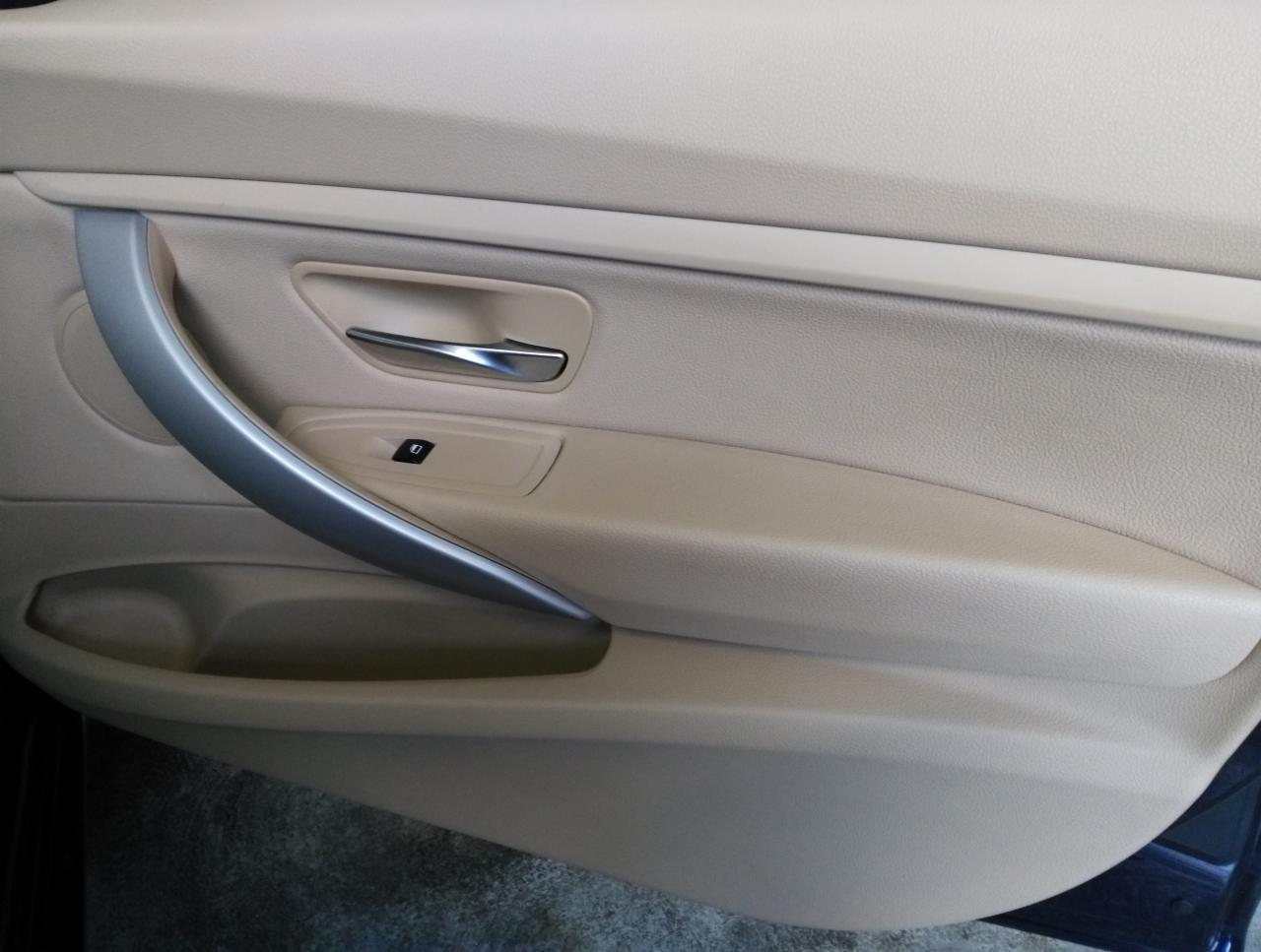 Wnętrze beżowych drzwi samochodu z chromowaną klamką i panelem sterowania szybami.
