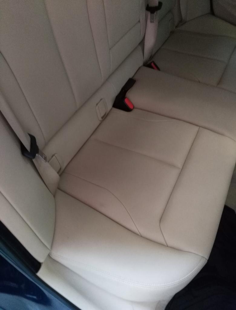 Jasna, skórzana tylna kanapa samochodu z widocznymi pasami bezpieczeństwa i zagłówkami.