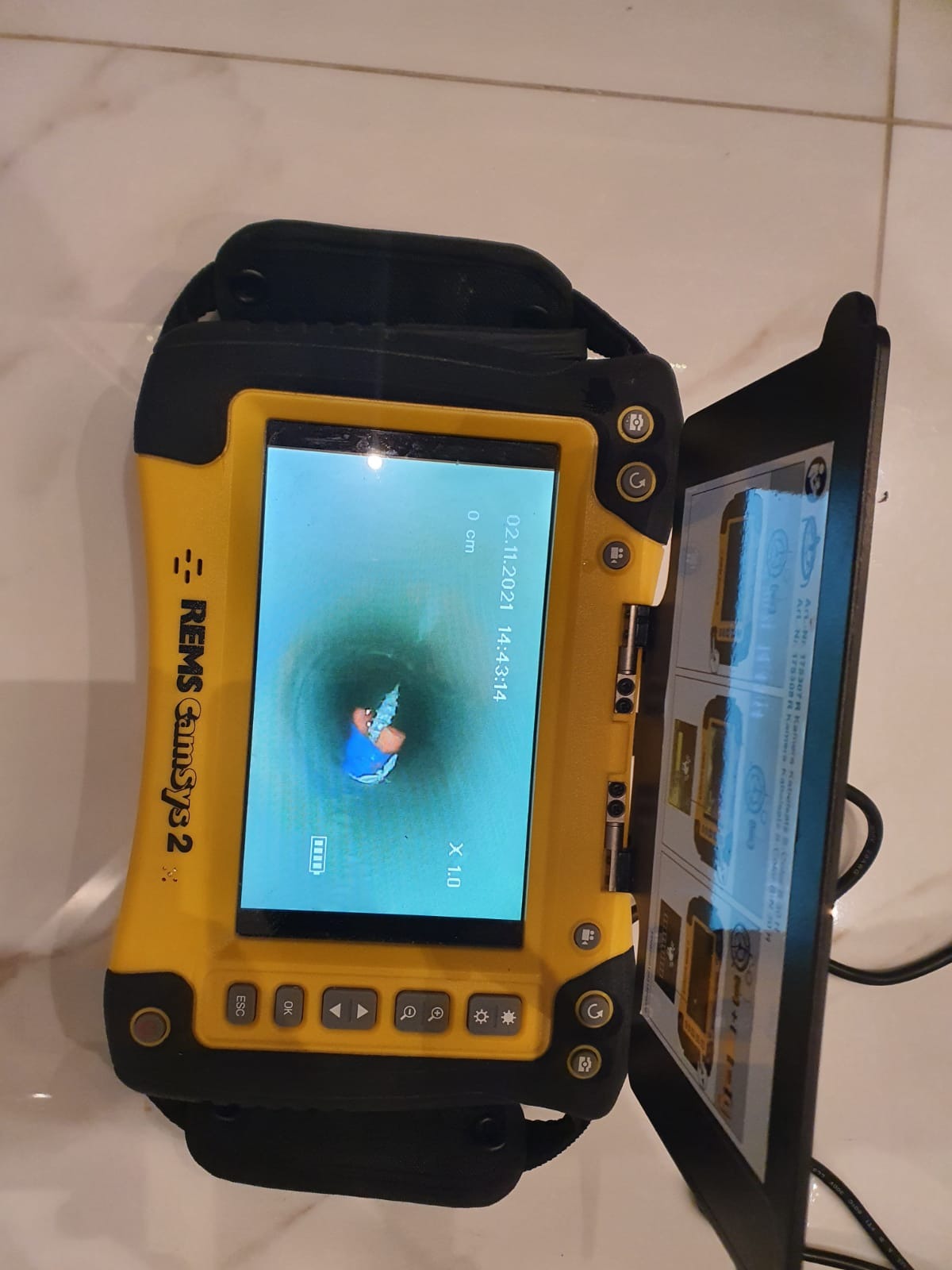 Żółte urządzenie inspekcyjne REMS CamSys 2 z otwartym ekranem pokazującym obraz z kamery wewnątrz rury, data i godzina na ekranie: 02.11.2021 14:43:14.
