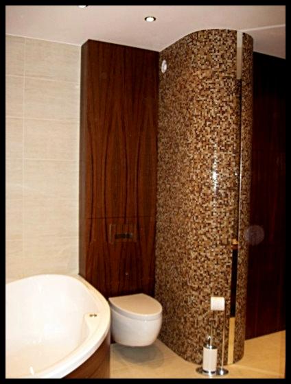 Nowoczesna łazienka z wanną, toaletą i kabiną prysznicową wykończoną mozaiką w odcieniach brązu, obok szafka z forniru w kolorze ciemnego drewna.