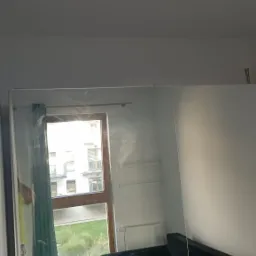 Pokój po remoncie, widoczny narożnik, okno z zieloną zasłoną i ślady po gładzi na ścianie