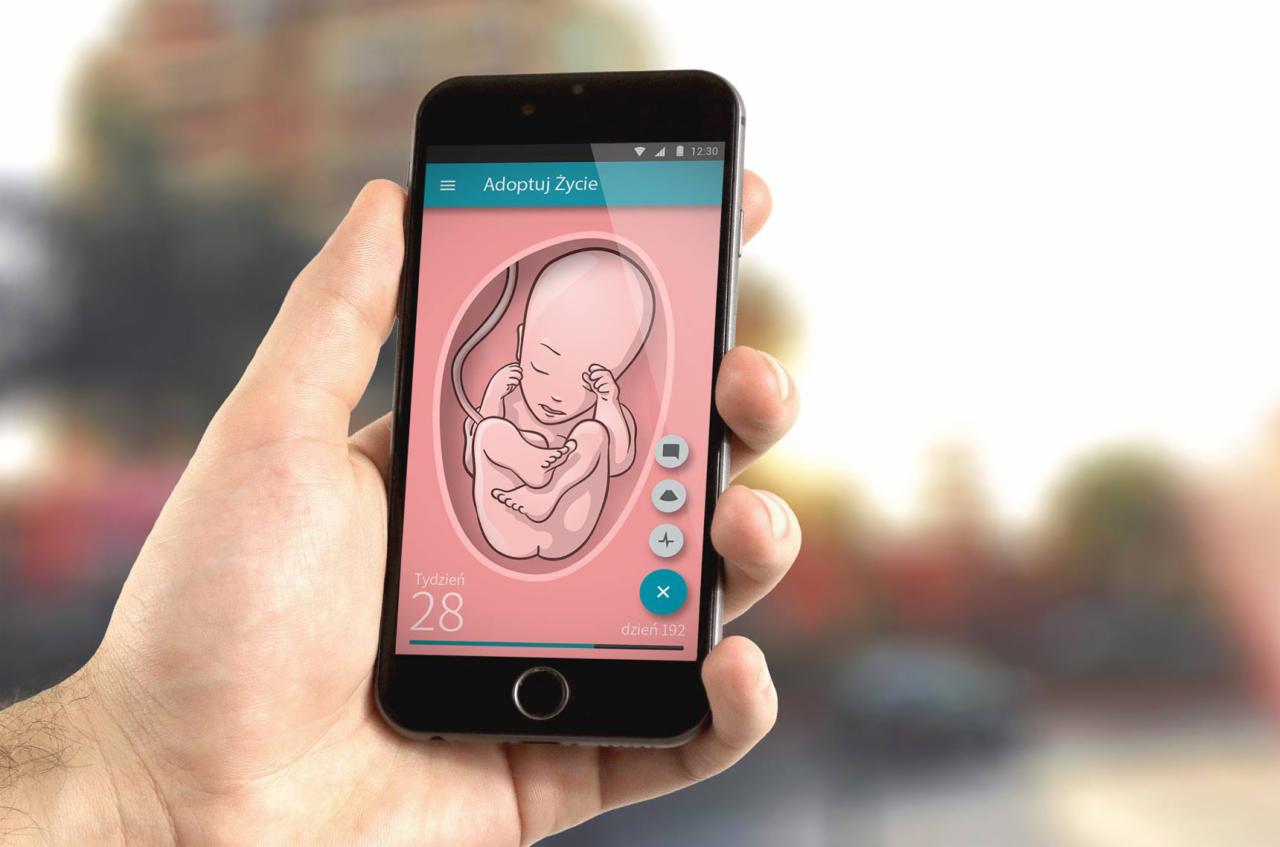 Dłoń trzyma smartfon z aplikacją prezentującą ilustrację 28-tygodniowego płodu w łonie matki, z interfejsem użytkownika w odcieniach różu i błękitu.