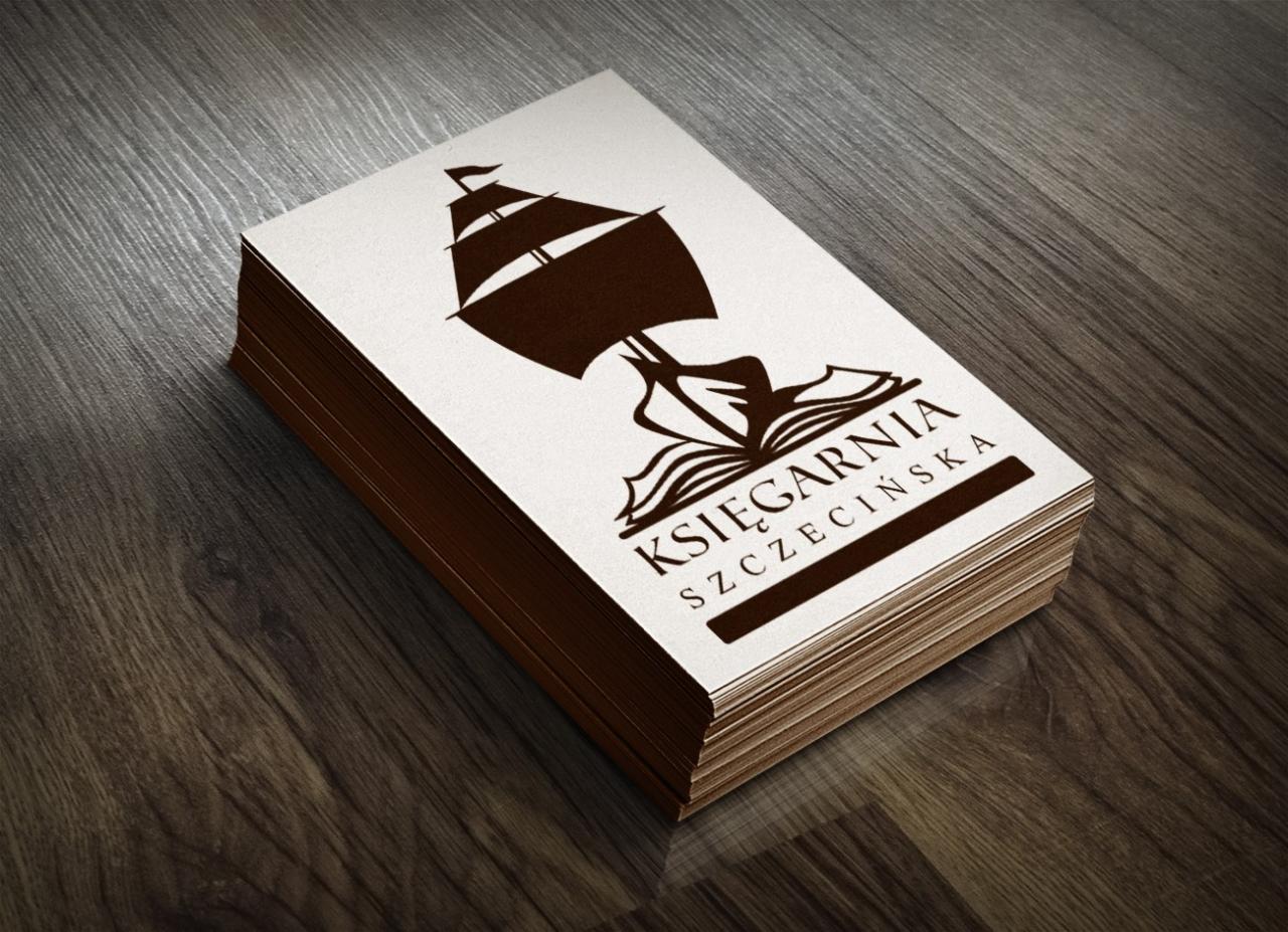 Stos wizytówek z logo księgarni: stylizowany żaglowiec wyrastający z otwartej książki, nazwa 'Księgarnia Szczecińska' na drewnianym tle.