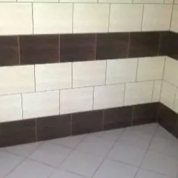 Wykończona łazienka z beżowo-brązowymi płytkami ułożonymi w poziome pasy na ścianach i jasnymi płytkami na podłodze, widok z narożnika.