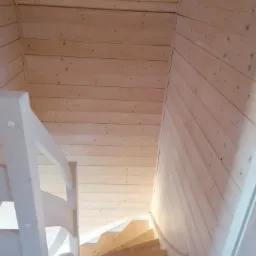 Drewniane schody kręcone w wykończonym wnętrzu z boazerii, biała balustrada, widok z góry.