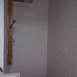 Nowoczesna kabina prysznicowa z drewnianym panelem, deszczownicą i ręczną słuchawką, wyłożona płytkami w odcieniach szarości z drewnianą podłogą.