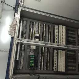 Otwarta szafa sterownicza z modułami PLC i okablowaniem, widoczne diody sygnalizacyjne, wnętrze szarej obudowy, instalacja w trakcie montażu.