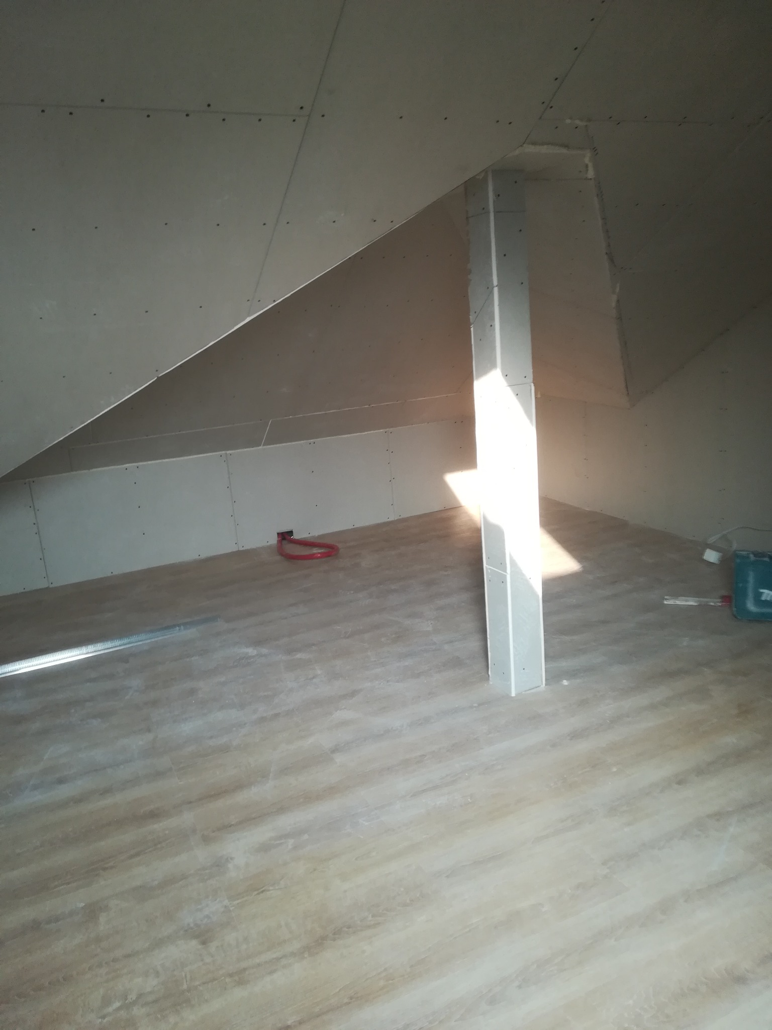 Poddasze w trakcie wykańczania płytami kartonowo-gipsowymi, widoczna konstrukcja nośna obudowana płytami, podłoga wyłożona panelami imitującymi drewno, fragment instalacji elektrycznej.