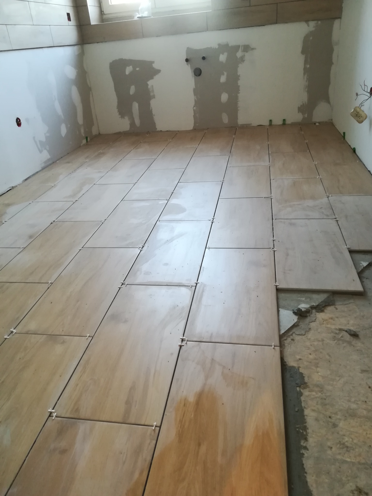 Układanie płytek podłogowych w trakcie remontu, widoczne krzyżyki dystansowe i niedokończone fragmenty podłoża.