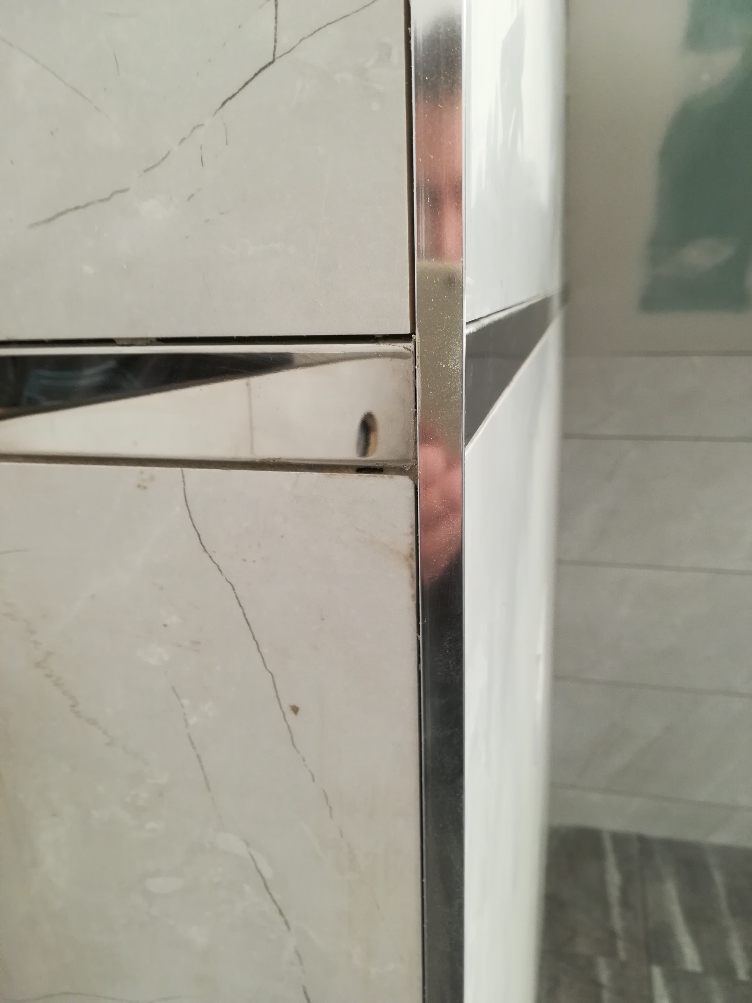 Detal montażu płytek imitujących marmur z metalową listwą wykończeniową w rogu, widoczny fragment ściany przygotowanej pod płytki.