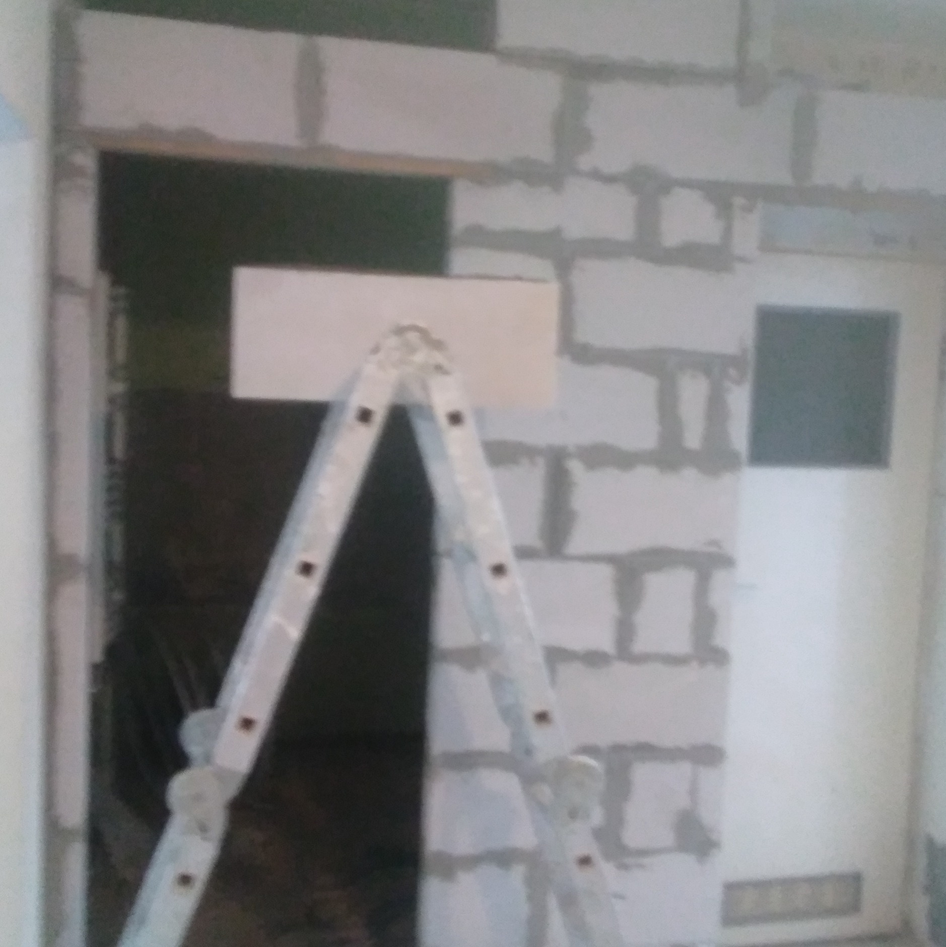 Wznoszenie ściany działowej z bloczków betonowych, widoczna drabina aluminiowa i przygotowany otwór drzwiowy.