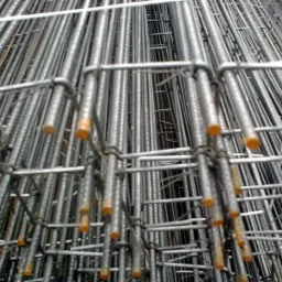 Siatka zbrojeniowa z prętów stalowych, widoczne pomarańczowe końcówki zabezpieczające, ułożona warstwami, perspektywa z dołu.