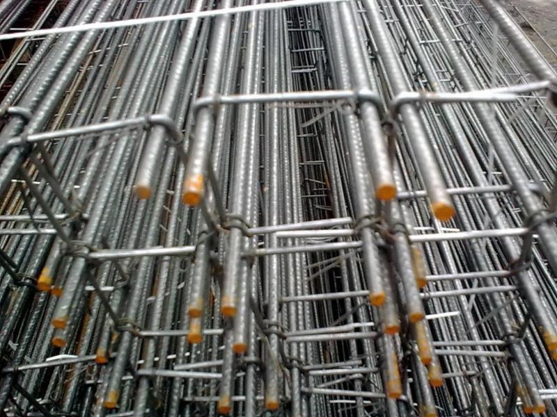 Siatka zbrojeniowa z prętów stalowych, widoczne pomarańczowe końcówki zabezpieczające, ułożona warstwami, perspektywa z dołu.