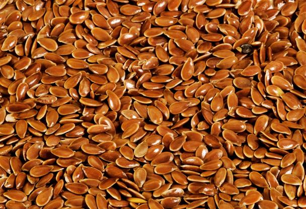 Widok z góry na brązowe nasiona lnu z jednym czarnym nasionem pośród nich.