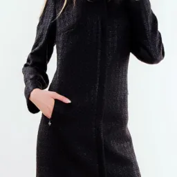 Kobieta prezentuje elegancki, ciemny płaszcz z teksturą, z ręką w kieszeni z ozdobnym suwakiem, na białym tle.