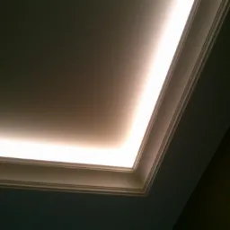 Sufit z oświetleniem LED wzdłuż listwy dekoracyjnej, skierowany w dół, z widocznym fragmentem pomalowanej ściany w tle.