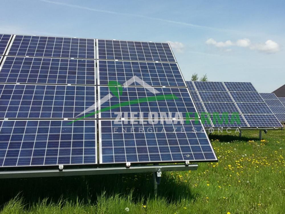 Rząd paneli fotowoltaicznych na łące z kwitnącymi mniszkami, z logo firmy 'Zielona Energia Słoneczna' na pierwszym planie.