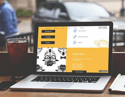 Laptop wyświetlający stronę internetową z motywem zwierzęcym, obok szklanka z napojem i notatnik na drewnianym stole w kawiarni.