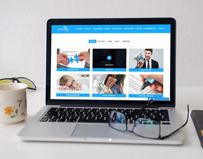 Laptop wyświetlający stronę internetową z różnorodnymi grafikami, okulary na klawiaturze, kubek z kwiatowym wzorem i książka obok, na białym biurku.