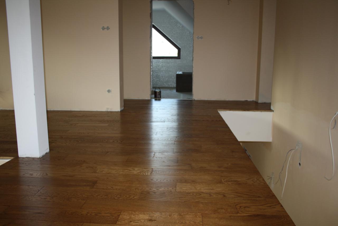 Ułożony parkiet z ciemnego drewna w pokoju z beżowymi ścianami, widoczna puszka z farbą i przejście do innego pomieszczenia.