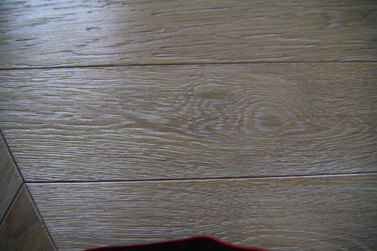 Jasne, lakierowane deski parkietowe ułożone w regularny wzór, widoczne słoje drewna i delikatny połysk lakieru.