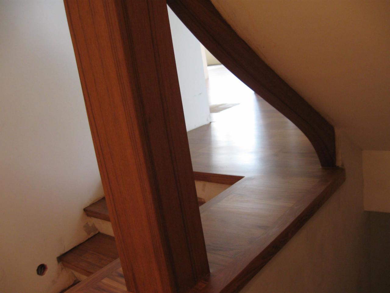 Drewniane schody z balustradą i słupkiem, wykończone parkietem w jasnym wnętrzu, widok z dołu.