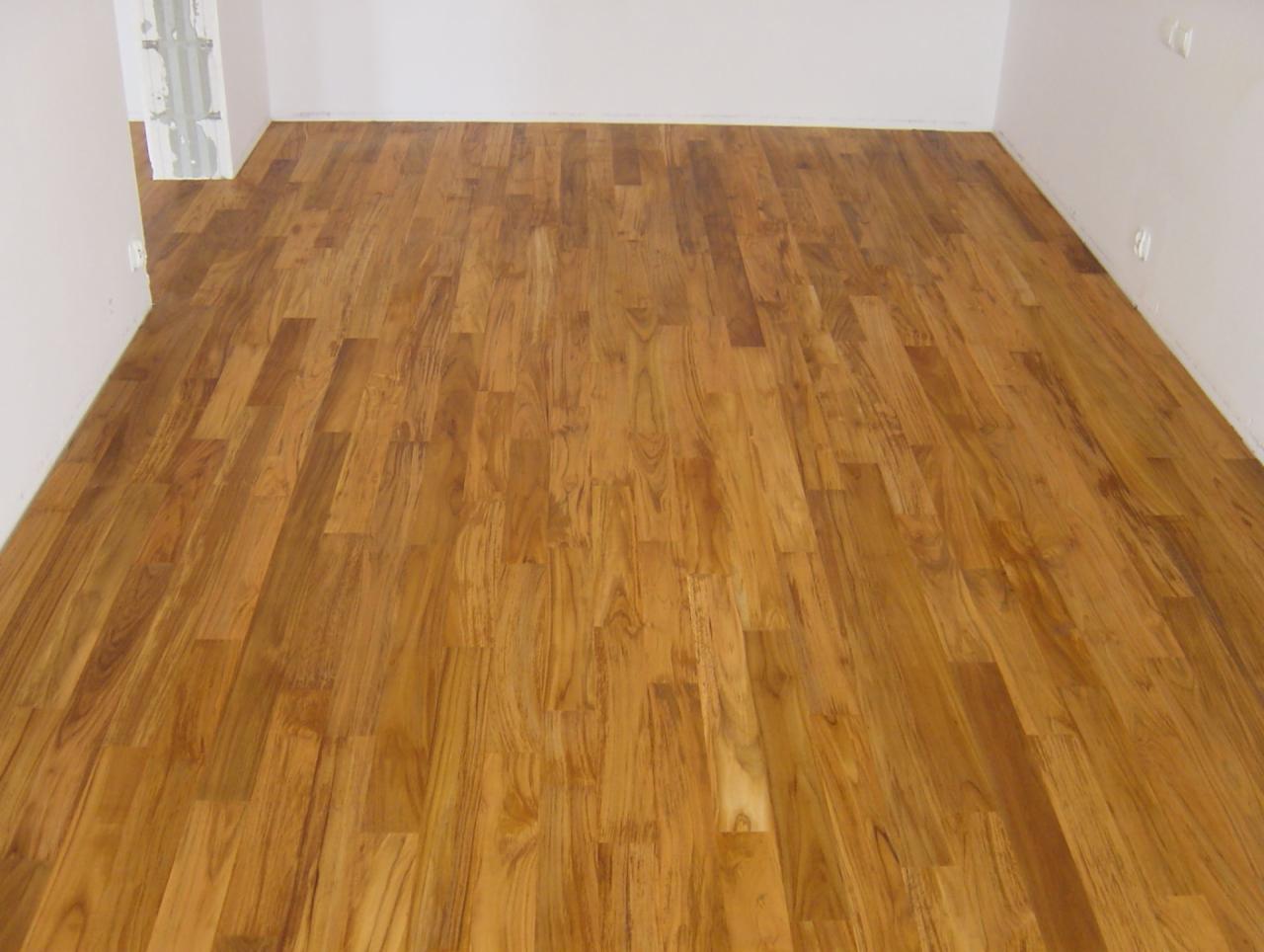 Świeżo ułożony parkiet z egzotycznego drewna w jasnym, pustym pokoju z białymi ścianami. Widoczny wzór słojów i naturalne odcienie brązu.