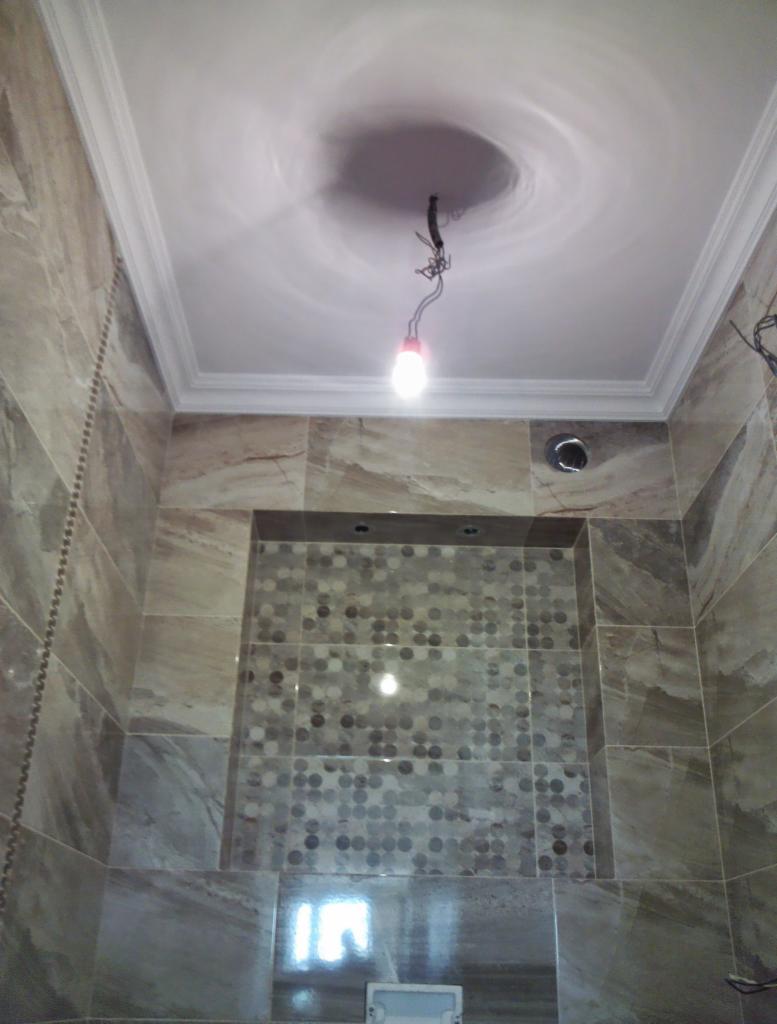 Łazienka w trakcie prac wykończeniowych, widoczne marmurowe płytki, mozaika w niszy, biały sufit z listwami dekoracyjnymi i wystającym okablowaniem oświetleniowym.