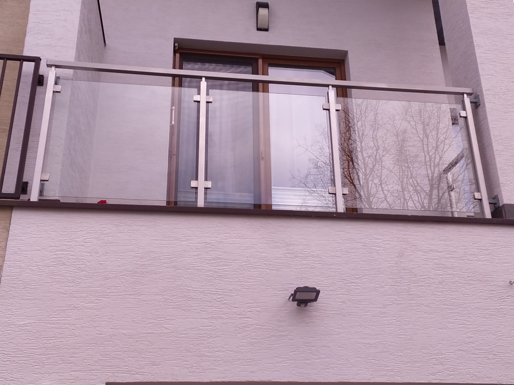 Szklana balustrada balkonowa z nierdzewnymi elementami mocującymi, zamontowana w Radomiu na tle białej elewacji budynku.