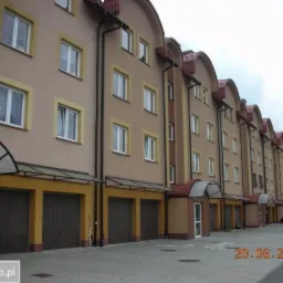 Elewacja szeregowca z garażami w kolorze beżowo-żółtym, z czerwonymi dachówkami, sfotografowana w pochmurny dzień.