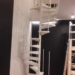 Montaż białych schodów spiralnych w nowym budynku, widoczna drabina i przygotowane ściany.