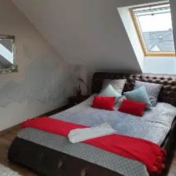 Sypialnia na poddaszu z łóżkiem, oknem dachowym i dekoracyjnymi panelami 3D na ścianie. Widoczne panele i lustro. Ściany skośne.