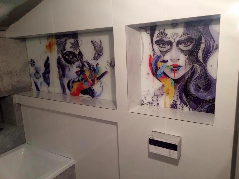 Dwa podświetlane panele szklane z abstrakcyjnymi portretami kobiet w niszy nad wanną w łazience. Portrety w odcieniach fioletu, bieli i czerni z akcentami kolorowych plam.