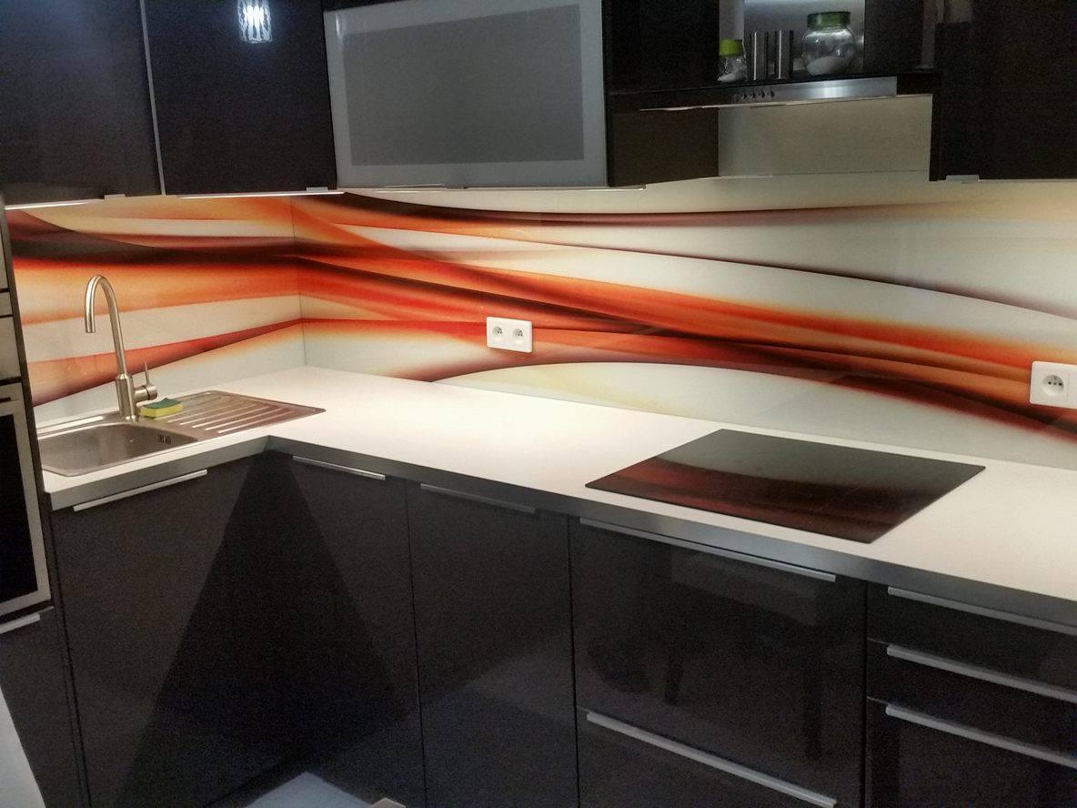 Szklany panel kuchenny z abstrakcyjnym wzorem w odcieniach bieli, pomarańczy i brązu, zamontowany nad blatem i płytą indukcyjną w nowoczesnej kuchni z ciemnymi szafkami.