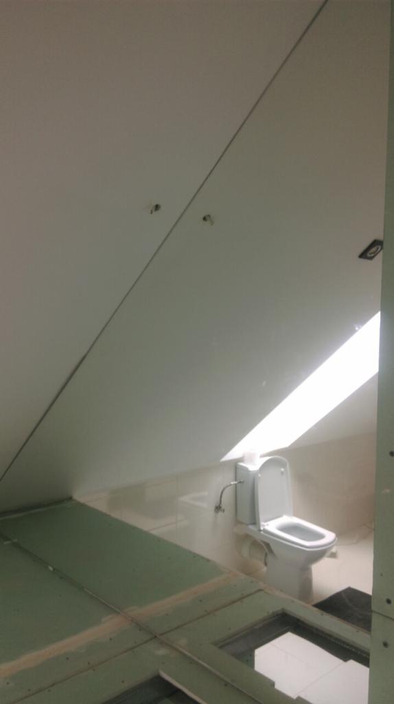 Poddasze w trakcie adaptacji na łazienkę: widoczny fragment podłogi z płyt gipsowo-kartonowych, na dalszym planie toaleta w jasnym pomieszczeniu ze skosem.