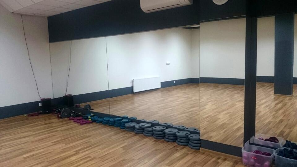 Ściana z lustrami w sali gimnastycznej, widoczne obciążenia i sprzęt do ćwiczeń ułożone wzdłuż ściany